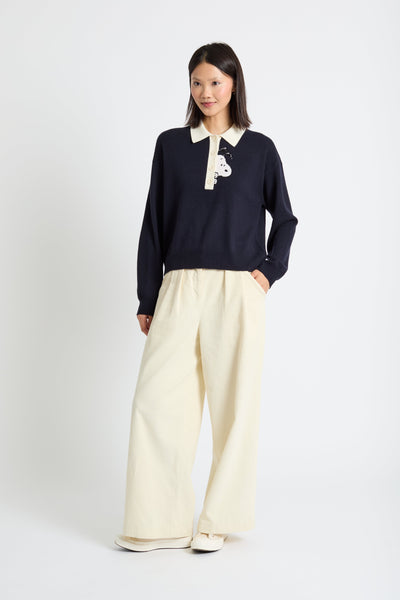 Woman wearing a navy sweater with a white collar and beige pants on a white background