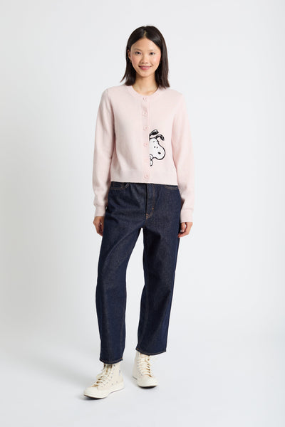 Person wearing a light pink sweater with a graphic design and dark jeans on a white background