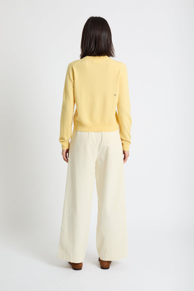 Person wearing a yellow sweater and white pants on a white background