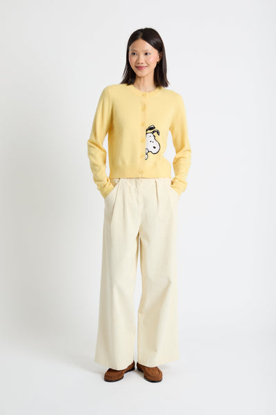 Woman wearing a yellow cardigan with a design and white pants on a white background