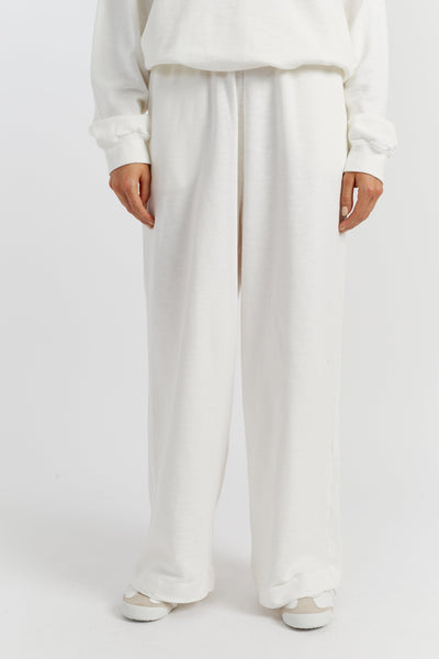 Person wearing a white outfit with wide-leg pants on a plain background