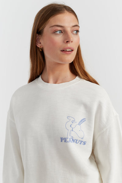 Woman wearing a white sweatshirt with a blue Peanuts logo on a light gray background