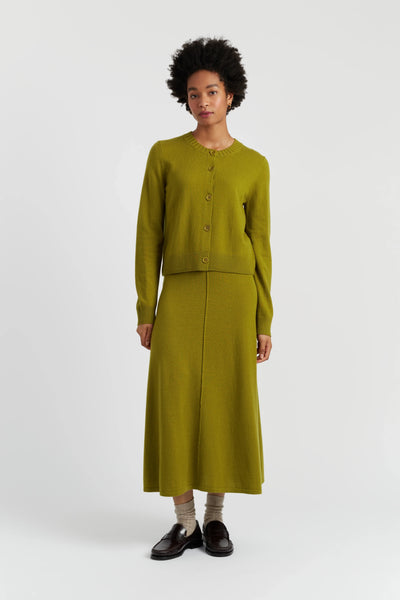 Person wearing a green cardigan and skirt set on a white background