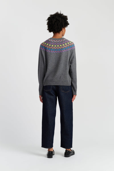 Person wearing a gray sweater with colorful patterns on the back, standing against a white background