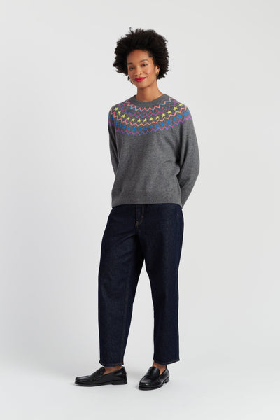 Person wearing a gray sweater with a colorful pattern and dark jeans on a white background